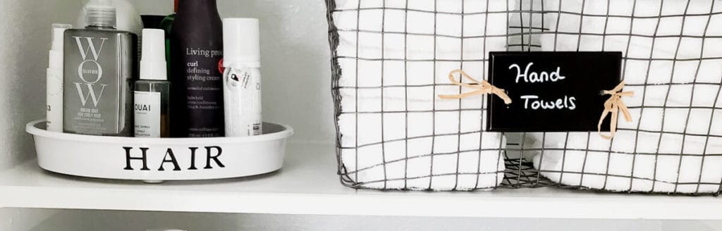 Hair products organized on a white plastic turntable and white hand towels neatly folded and stored in a pretty wire basket in a neatly organized linen closet