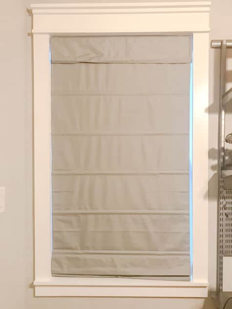 A white trimmed window with a gray fabric roman shade looks great when organizing kid's bedroom
