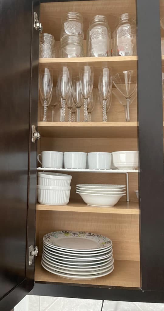 An organized kitchen cabinet with plates, bowls, champagne flutes, and mason jars.