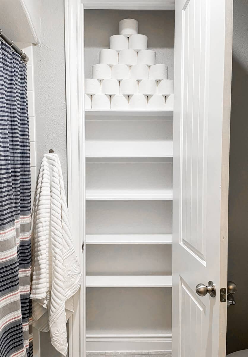 A freshly painted closet with a pyramid of toilet paper on the top shelf