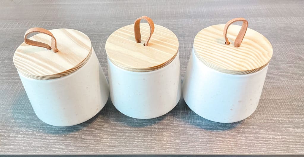 3 white glass jars with bamboo lids sitting on a gray desk