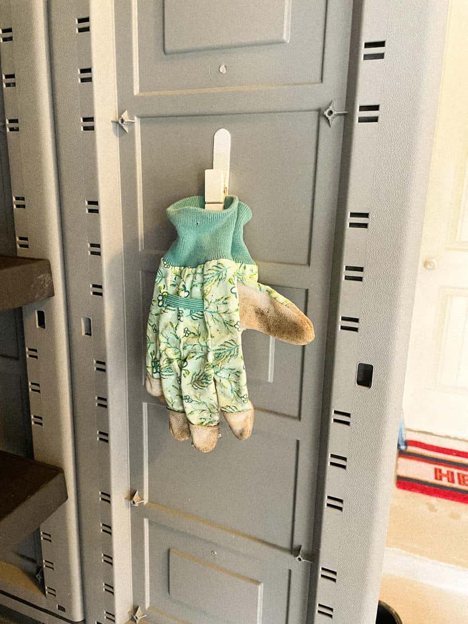 A pair of garden gloves hanging on a command hook inside a garage storage cabinet