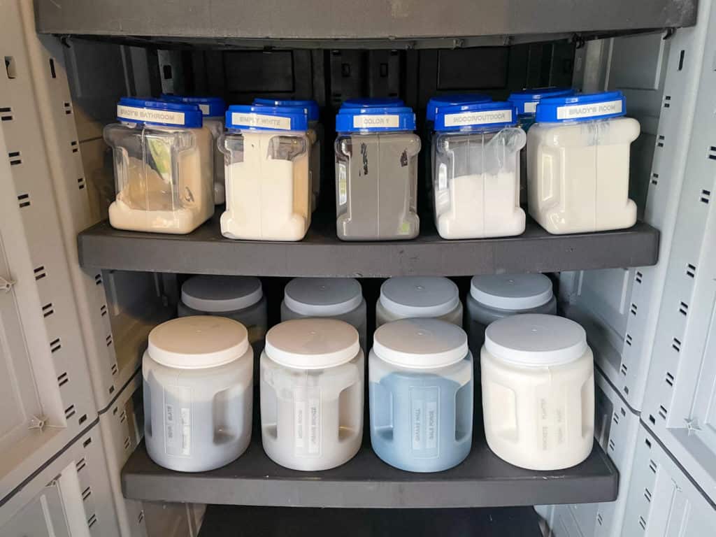 Clear plastic containers filled with paint inside a garage storage cabinet