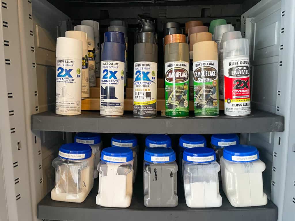 Spray paint cans organized with other containers of paint inside a garage storage cabinet