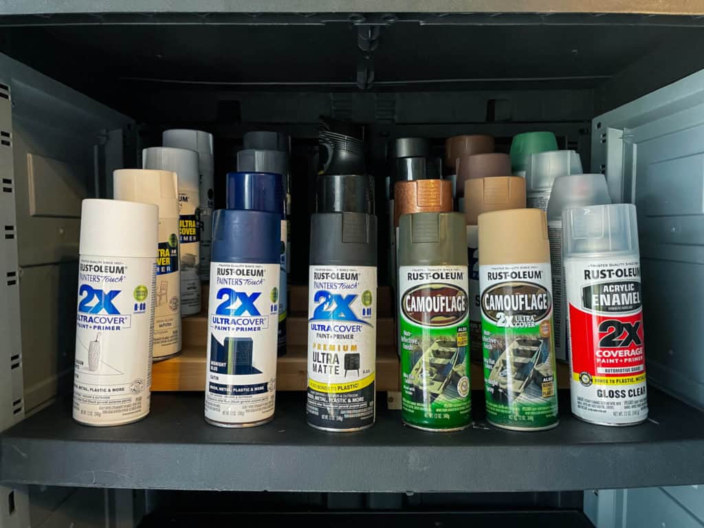 Several cans of spray paint organized inside a garage storage cabinet