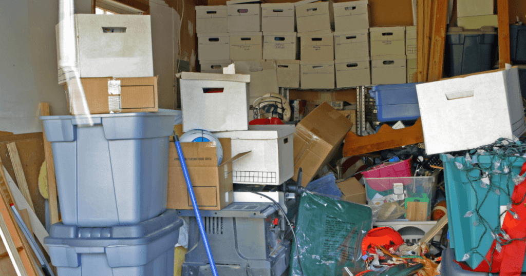 A very mess garage with stacks of boxes, bins, and miscellaneous items.