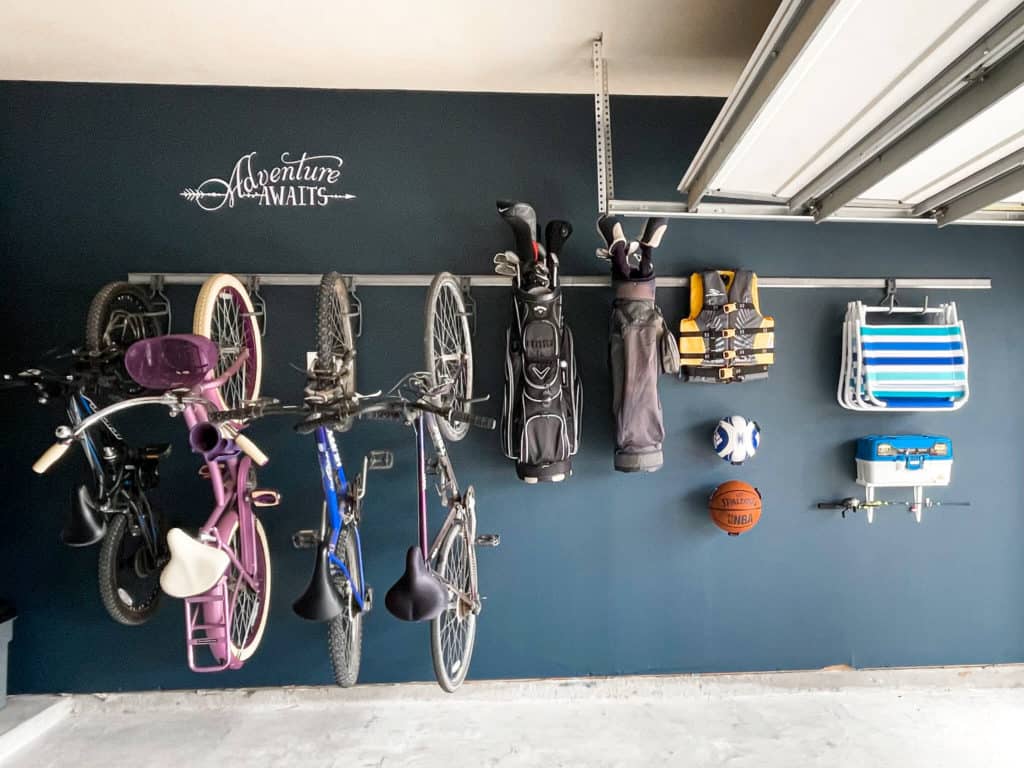 A track om a wall in a garage that holds bikes, golf bags, and other garage items