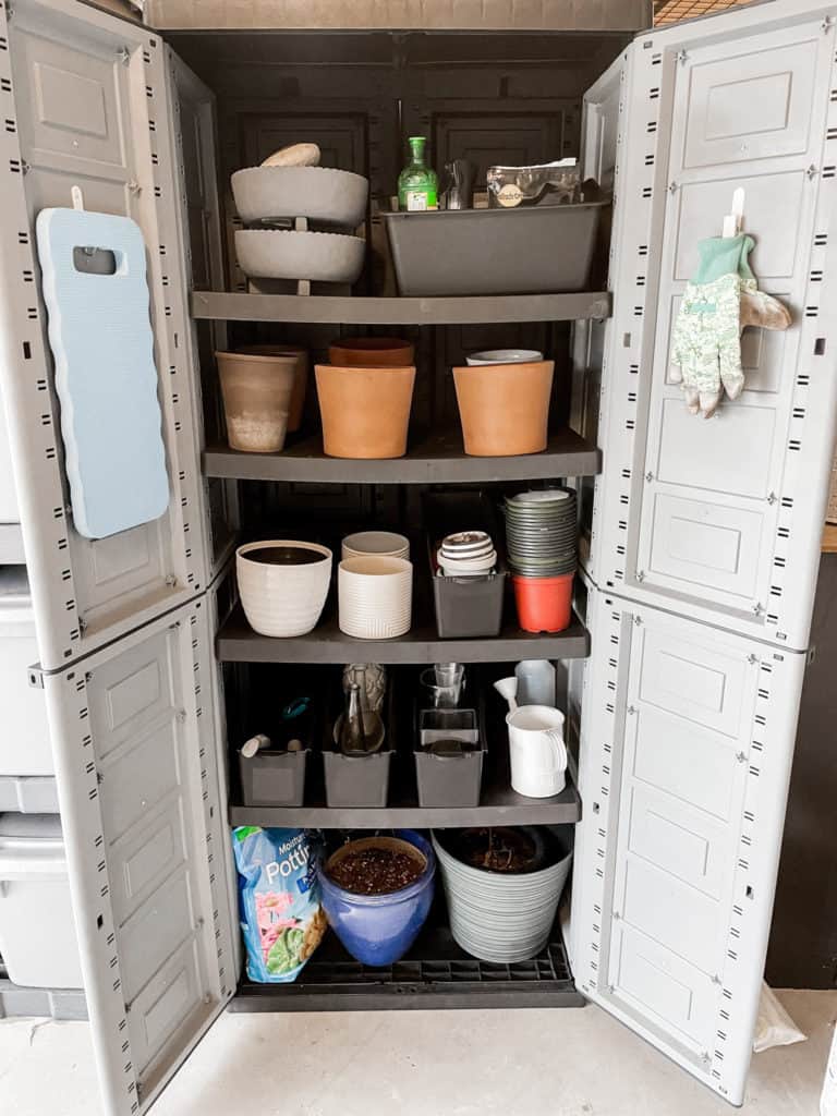 A garage storage cabinet holding gardening equipment, tools, and pots